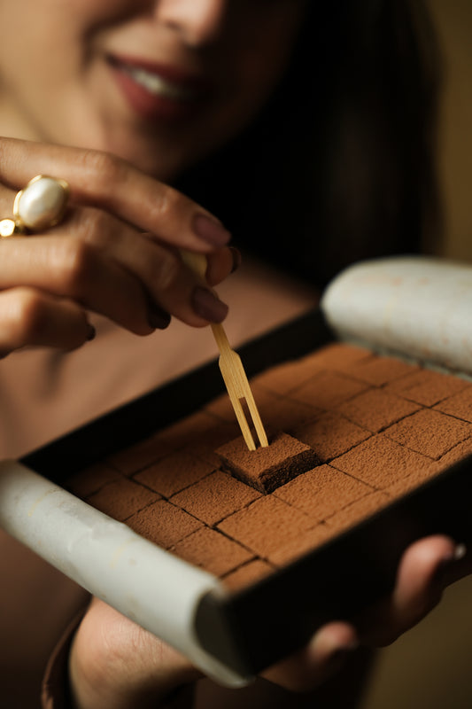 Woman lifting a cocoa-dusted ganache square from a Ganache de Luxe box